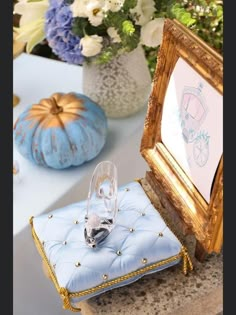 an empty glass sits on a blue cushion next to a gold frame and some flowers