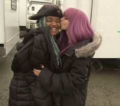 two women standing next to each other in front of a white trailer and one is kissing the other