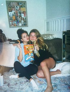 two young women sitting on a bed and one is holding a drink in her hand