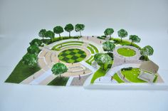 a paper model of a park with trees and grass in the center, on top of a white surface