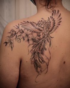 the back of a woman's shoulder with a bird and flowers tattoo on it