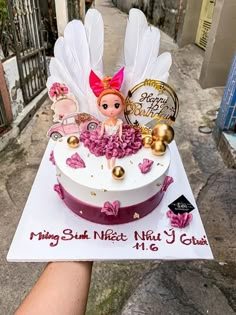 a birthday cake with a doll on top is being held by someone's hand