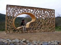 a man sitting on top of a wooden sculpture in the middle of a dirt field