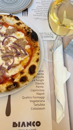 a pizza sitting on top of a white plate next to a glass of wine and silverware