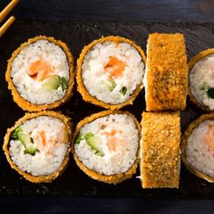 several sushi rolls on a black plate with chopsticks