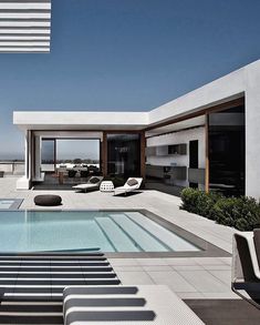 an outdoor swimming pool with lounge chairs next to it and the ocean in the background