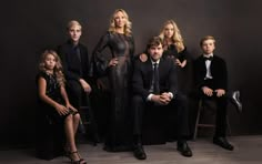 a group of people sitting next to each other in front of a dark background with one man wearing a tuxedo