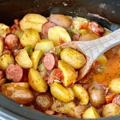 a wooden spoon in a slow cooker filled with potatoes and sausage