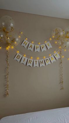 a birthday banner with balloons and streamers on the wall next to a white bed