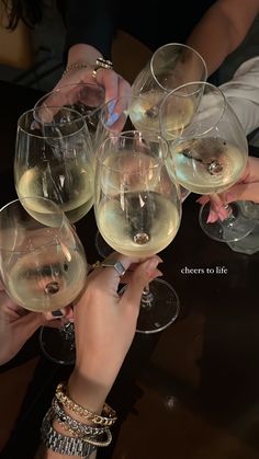 several people are holding wine glasses with white wine in them and toasting each other