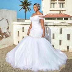 a woman in a white wedding dress standing on a roof with palm trees behind her