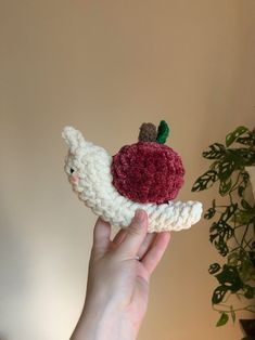 a hand holding a small crocheted apple on top of a piece of fruit