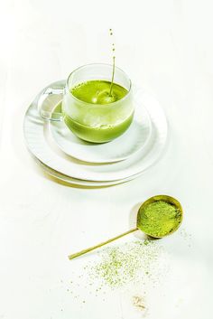 a spoon with matchsticks on it next to a cup filled with green liquid