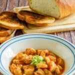 a bowl filled with pasta and bread on top of a wooden table next to sliced bread