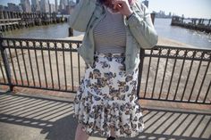 a woman in a skirt and jacket is talking on her cell phone near the water