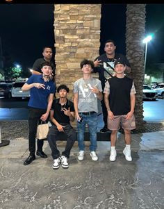 five young men posing for a photo in front of a tall stone column at night