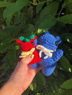 someone holding two crocheted toy animals in their hands, one is blue and the other is red