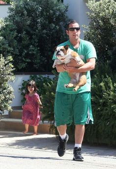 a man carrying a small dog in his arms while walking down the street with another person behind him