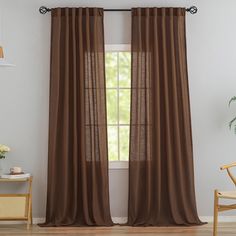 a brown curtain hanging in front of a window with a wooden chair and potted plant