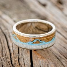 a wooden ring with blue and brown inlays sitting on top of a piece of wood