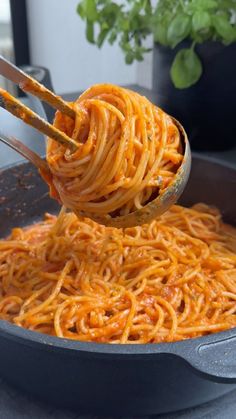 spaghetti being cooked in a skillet with tongs