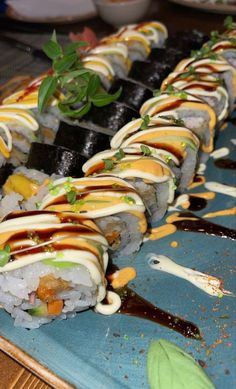 sushi rolls with sauce and garnish are on a blue platter, ready to be eaten