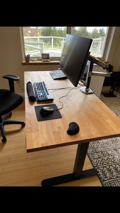 a wooden desk with a computer monitor and keyboard sitting on top of it next to a black chair