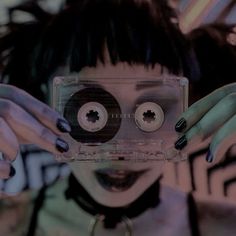 a woman holding up a cassette in front of her face with two hands on top of it