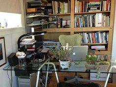 a glass desk topped with a laptop computer next to a book shelf filled with books