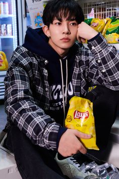 a young man sitting on top of a counter holding a bag of chips