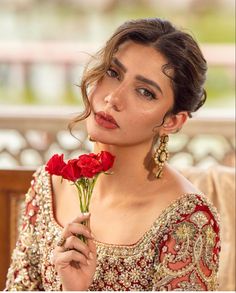 a woman in a red and gold dress holding a flower with her right hand on her hip