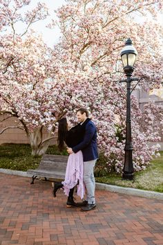 a man and woman standing next to each other in front of a tree with pink flowers