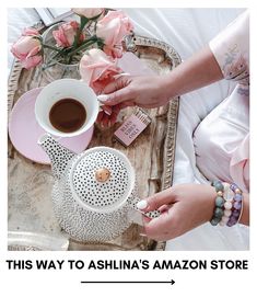 a woman holding a cup of coffee next to a tray with pink roses on it