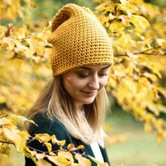 a woman wearing a yellow knitted hat looking down at her cell phone in front of some leaves