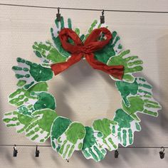 a handprint wreath hanging on the wall with red ribbon and green hands painted on it