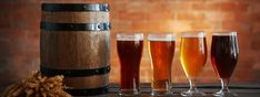 four different types of beer in glasses next to a barrel