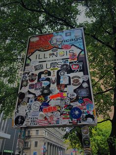 a street sign covered in lots of stickers on the side of a tree lined street