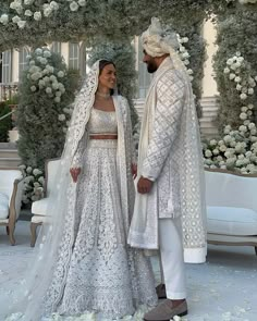 two people standing next to each other in front of a white flower covered arch with flowers