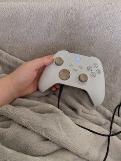 a person is holding a controller for a video game system in their hand on a blanket