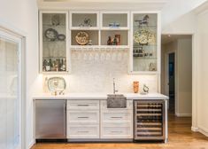 a kitchen with white cabinets and lots of wine glasses on the shelves above the sink