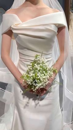 a woman in a white wedding dress holding a bouquet of flowers and wearing a veil