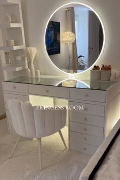 a white vanity with a round mirror and lights on it's side, in front of a bed