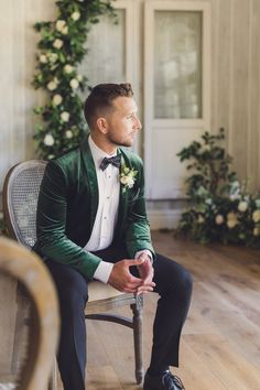 a man sitting in a chair wearing a green jacket and bow tie with flowers on the wall behind him