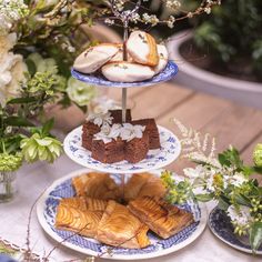 three tiered plates with pastries on them and flowers in vases next to each other