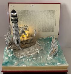 an open book with a lighthouse and boat on it, sitting on top of a table