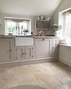 a kitchen with white cabinets and beige flooring is pictured in this image, there are two windows above the sink