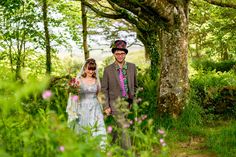 a man and woman dressed in period clothing walking through the woods with wildflowers