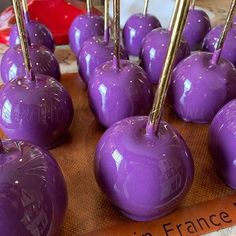 there are many purple candy apples on the wooden board with gold sticks sticking out of them