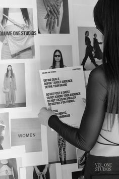 a woman standing in front of a wall with pictures on it and holding a piece of paper