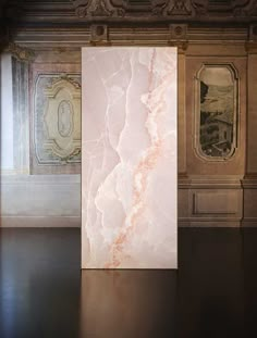 a large pink marble block sitting on top of a wooden floor next to two paintings